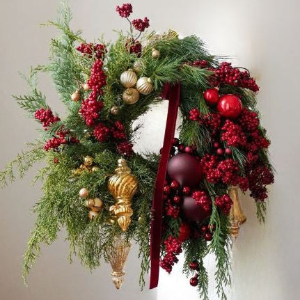 Decorative Christmas wreath with greenery, red berries, gold ornaments, and a red ribbon on a neutral background.