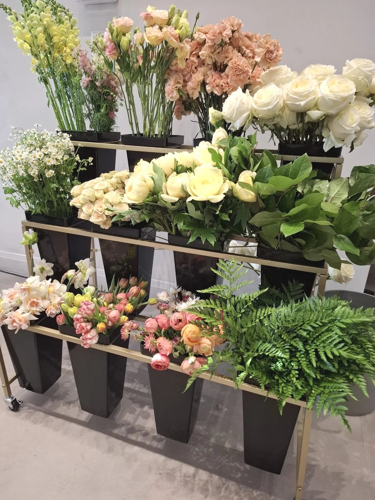 Display of various florals in a flower bar on a metal stand with a neutral background.
