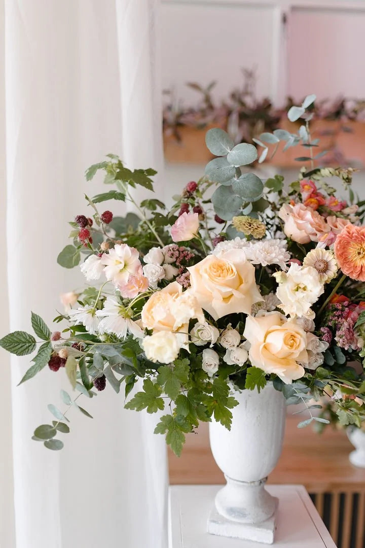 Floral arrangement in a white vase on a table with a blurred indoor background