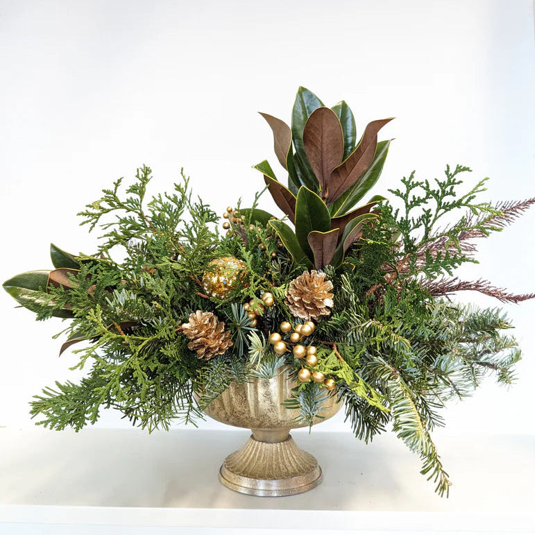 Decorative floral arrangement with greenery and gold elements in a silver vase on a white background